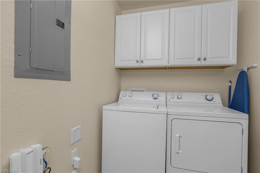 Laundry room with white washer and dryer beneath wall cabinets.