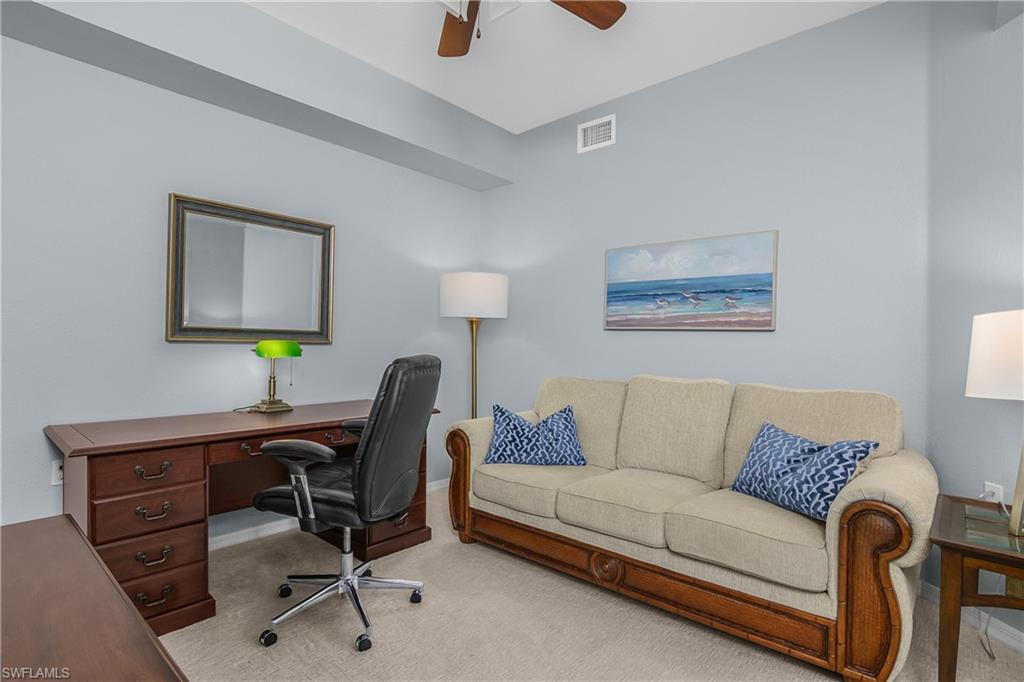 Furnished home office with a dark wood desk and black chair beside a beige sofa with blue pillows.