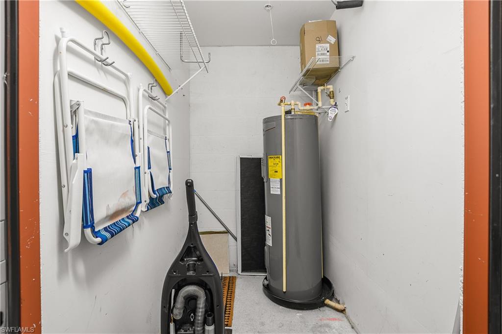 Utility closet with a tall water heater, wall-mounted folding chairs, and a vacuum.