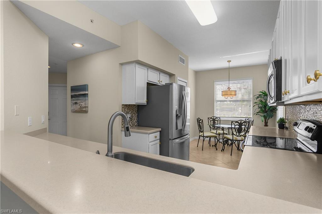 Kitchen with white cabinets, stone counters, stainless steel appliances, and a dining area by the window.