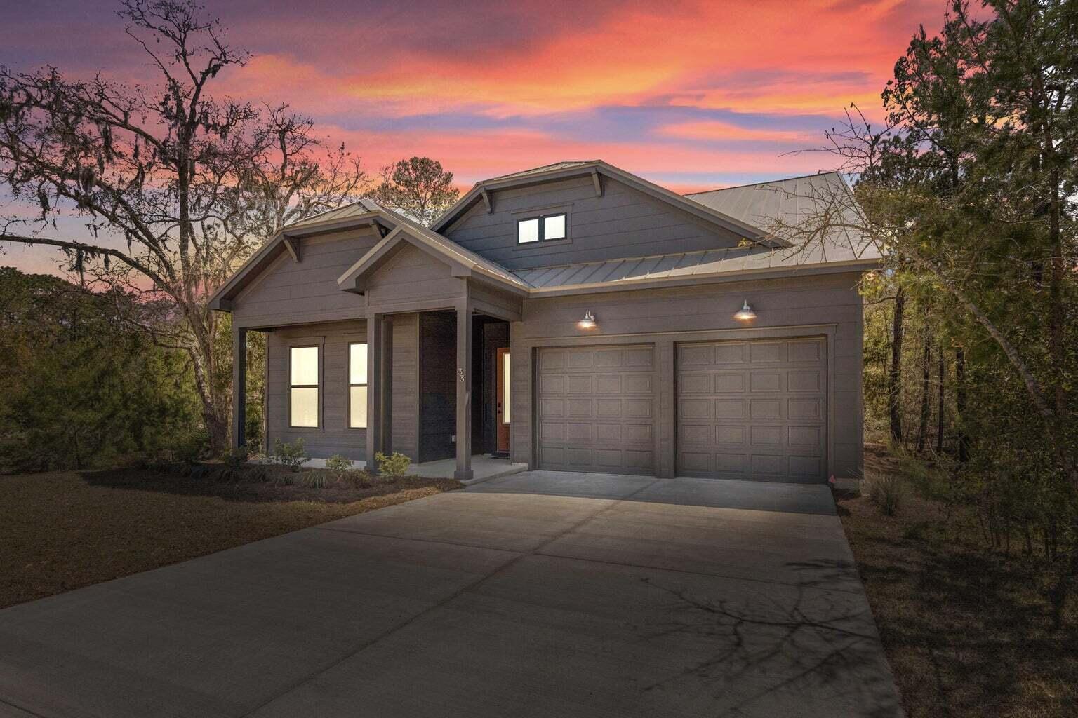 Gray single-story home with a two-car garage beneath a vivid pink and orange sunset.