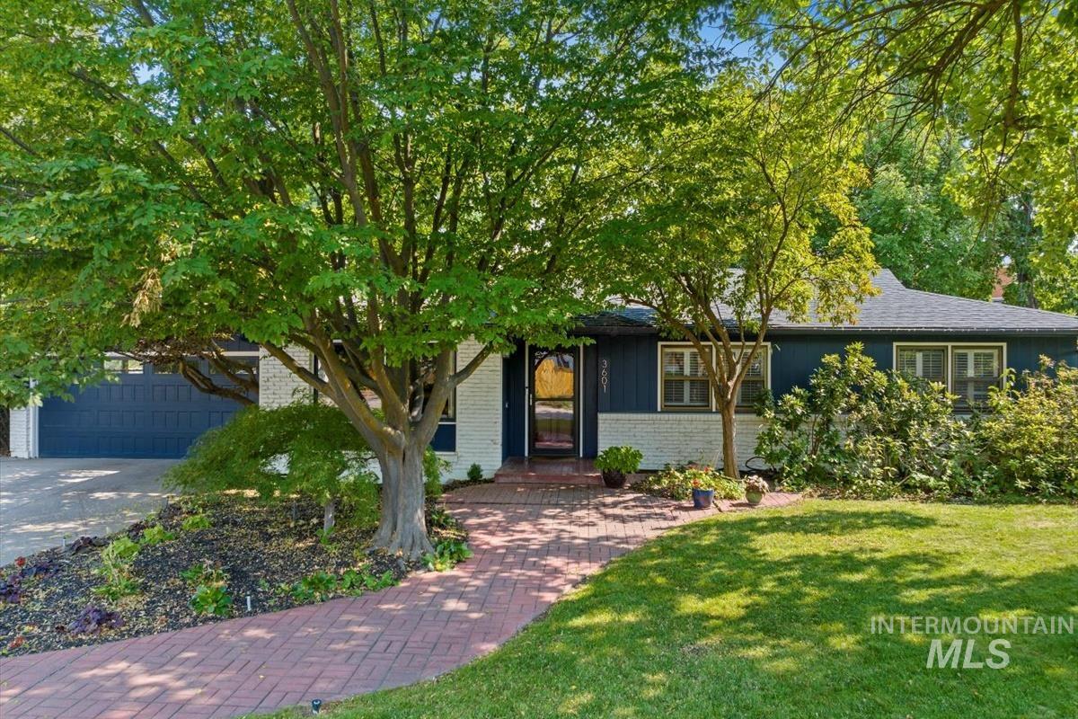 Single-story home with blue-and-white siding, mature trees, and a brick walkway to the entrance.