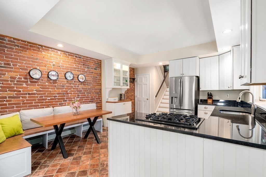 Kitchen with a black stone island and gas cooktop beside a dining nook and exposed brick wall.