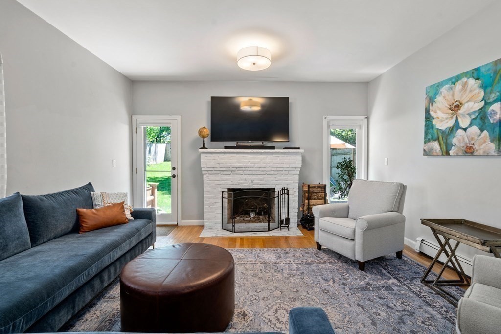 Living room with a white brick fireplace, dark blue sofa, gray armchair, and garden-facing glass doors.