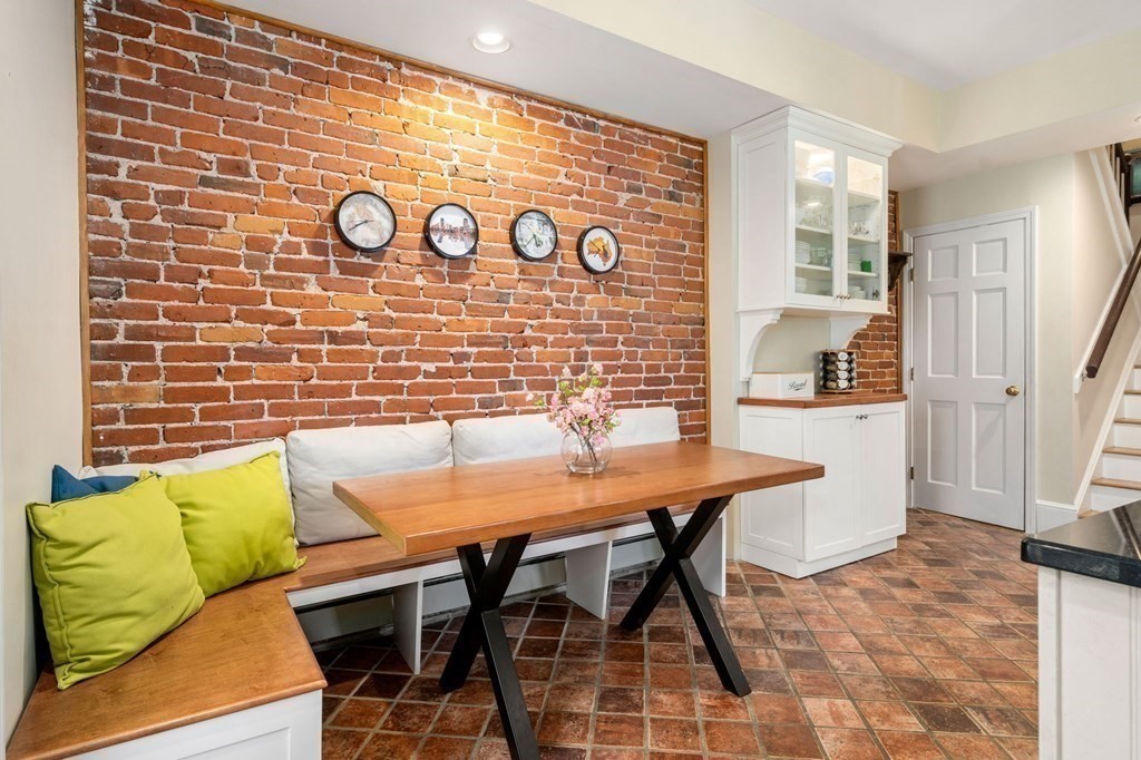 Dining nook with exposed brick, a wooden banquette, and green cushions.