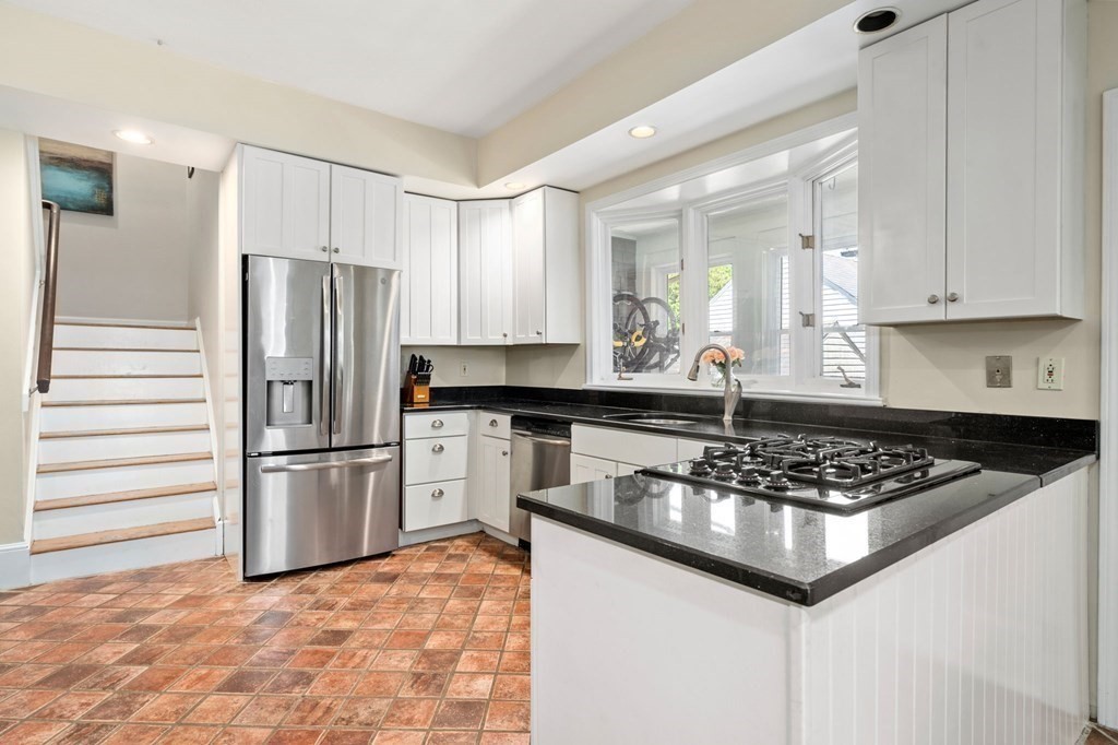 Kitchen with white cabinets, black countertops, a gas cooktop peninsula, and terracotta tile floor.