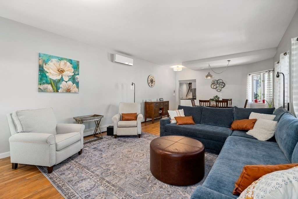 Living room with a blue sectional, white armchairs, leather ottoman, and dining area beyond.