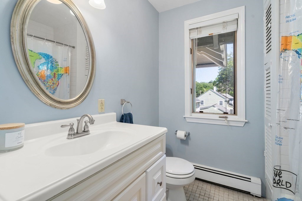 Bathroom with white vanity, oval mirror, and a world-map shower curtain beside the window.