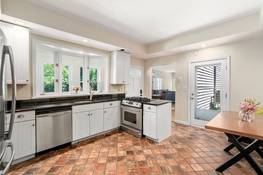 Kitchen with white cabinets, black countertops, stainless steel appliances, and a large window overlooking greenery.