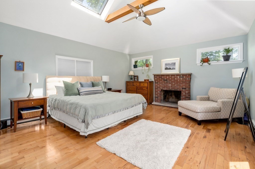 Bedroom with a vaulted ceiling, skylight, brick fireplace, hardwood floors, and sitting chair.