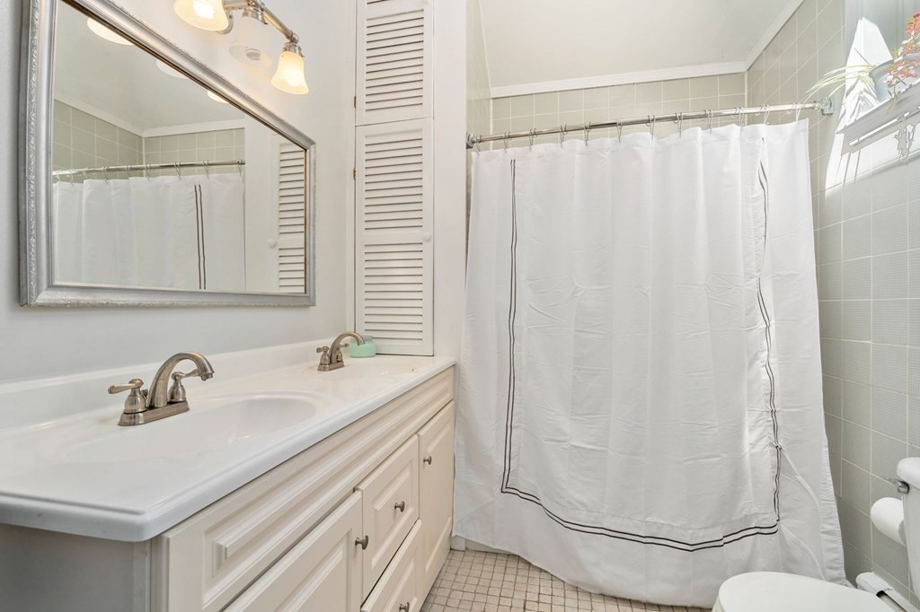 Bathroom with a double-sink vanity, large mirror, and white-curtained tiled shower.