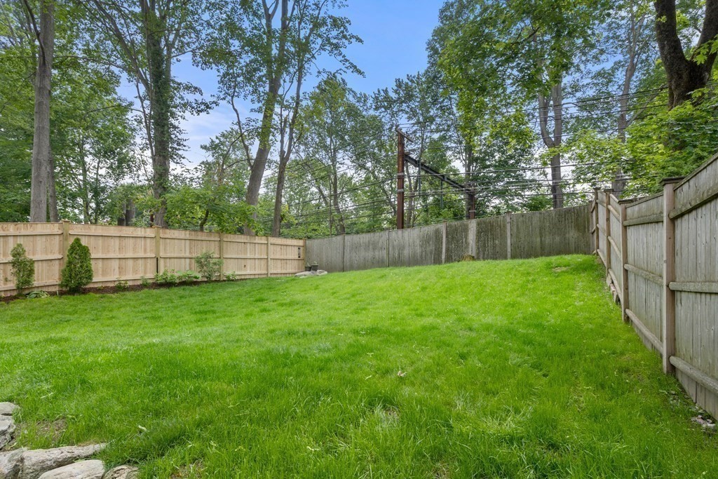 Grassy backyard enclosed by wooden fences, with mature trees and stone edging.