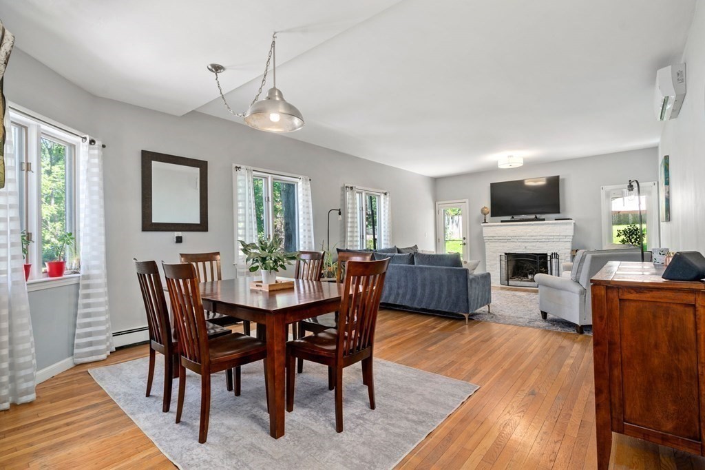 Open-plan living and dining room with hardwood floors and a white brick fireplace.