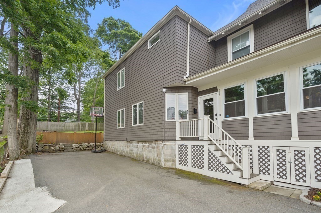 Gray-shingled home with white porch steps beside a paved driveway and basketball hoop.