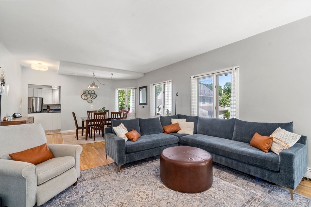 Living room with a large gray sectional, round leather ottoman, and dining area beyond.