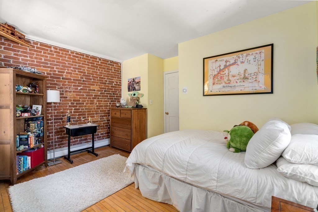 Bedroom with an exposed brick wall, hardwood floors, and a white bed.