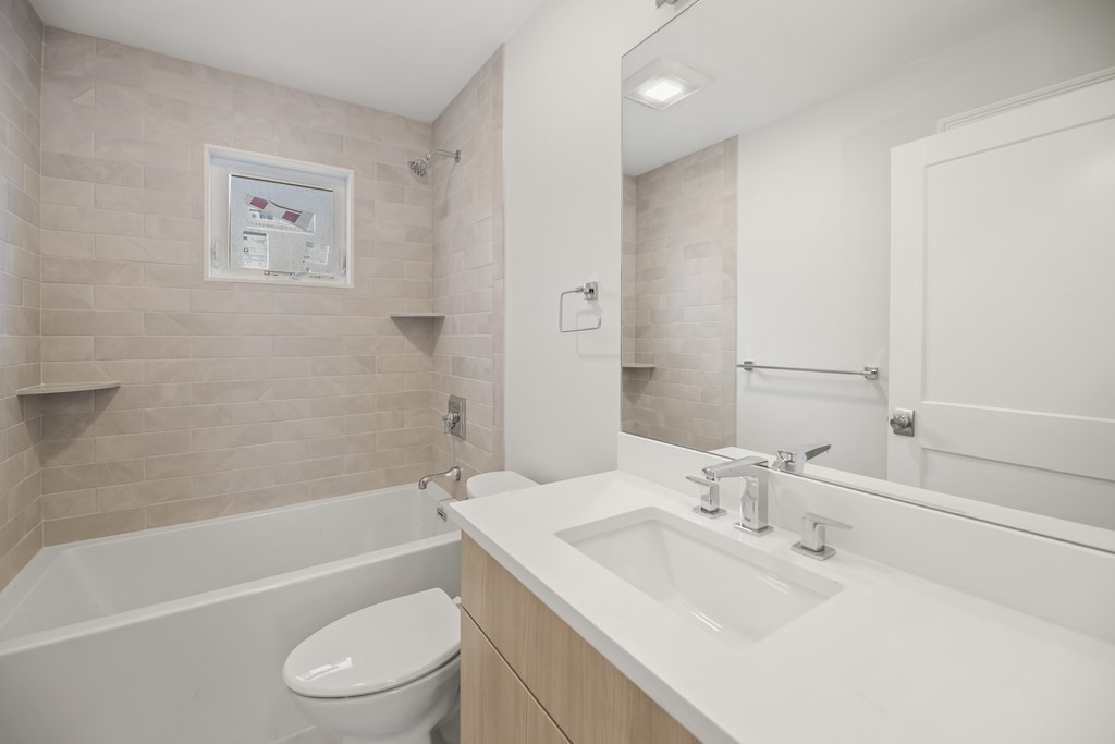 Bathroom with beige tiled tub surround and a light wood vanity with a white sink.