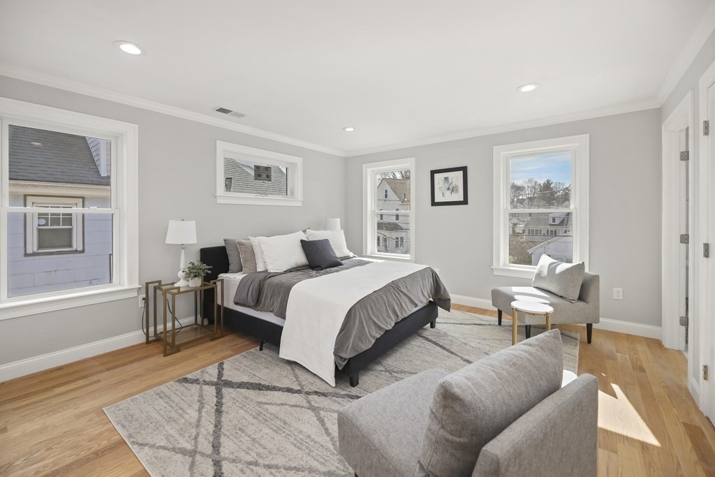 Staged bedroom with a large bed, hardwood floors, and several windows.
