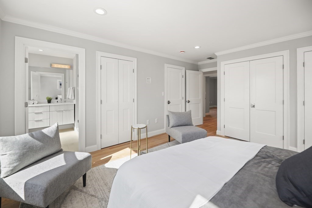 Furnished bedroom with gray seating, white paneled closets, and an adjoining vanity area.