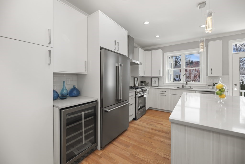 Modern white kitchen with a large island, stainless steel appliances, and warm wood floors.