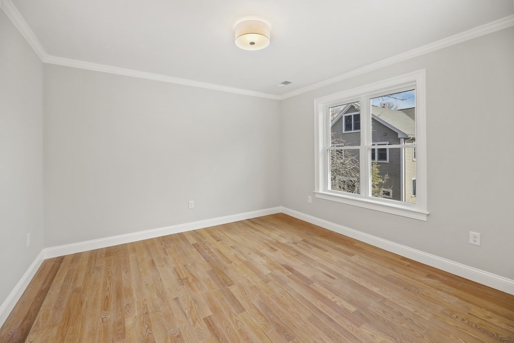 Empty room with hardwood floors and a large window overlooking a neighboring house.