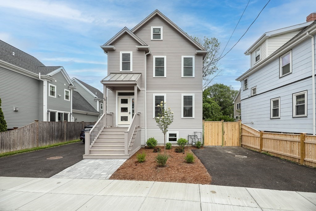 Gray multi-story home with a raised entry, paved driveways, and fenced side yards.