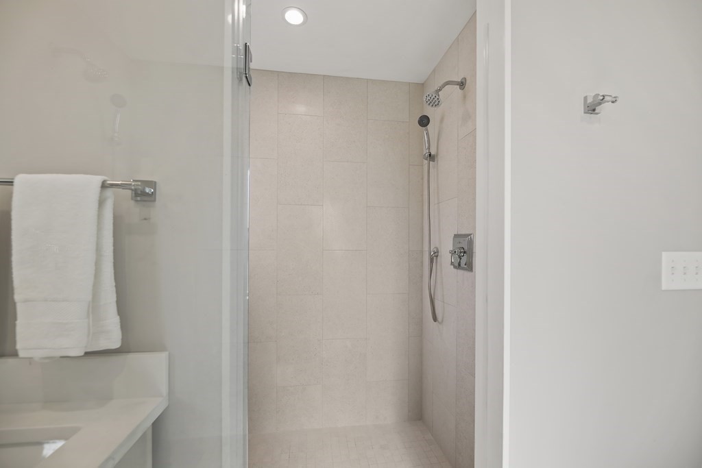 Bathroom with a glass-enclosed tiled shower and rainfall and handheld showerheads.