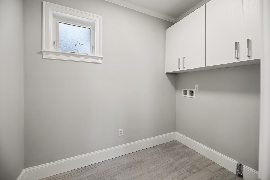 Empty laundry area with white cabinets, laundry hookups, a small window, and gray plank flooring.