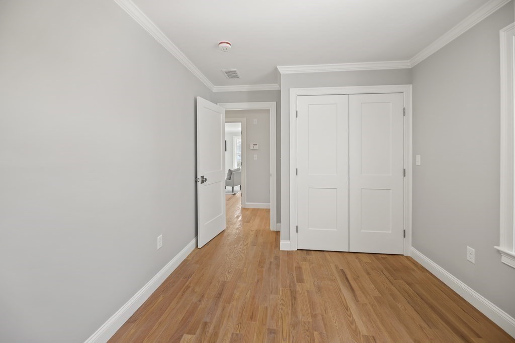 Empty room with hardwood floors, white double closet doors, and an open doorway to the hall.