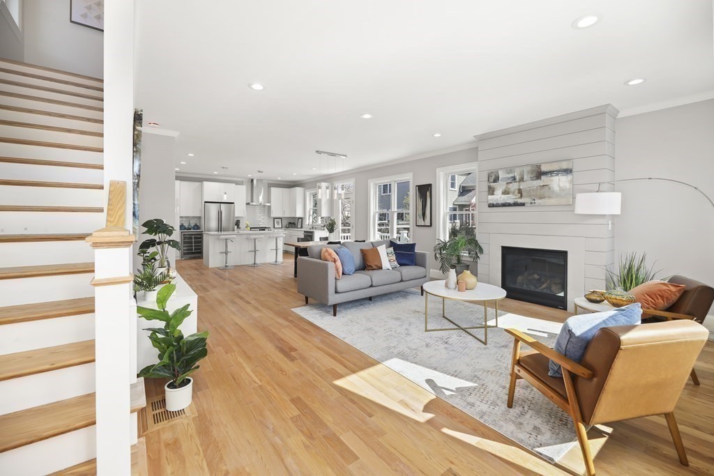 Open-plan living room with a gray fireplace, hardwood floors, and kitchen beyond.