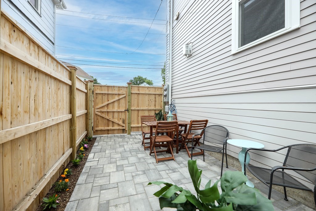 Paved patio with a wooden privacy fence, outdoor dining set, lounge chairs, and flower bed.