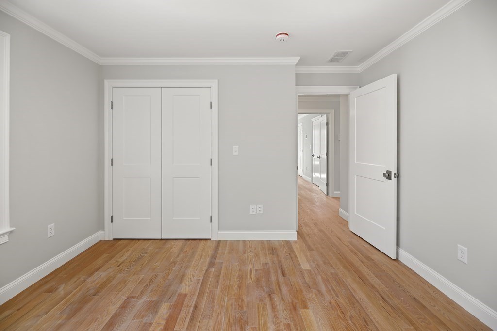 Vacant bedroom with hardwood floors, a double-door closet, and an open hallway door.