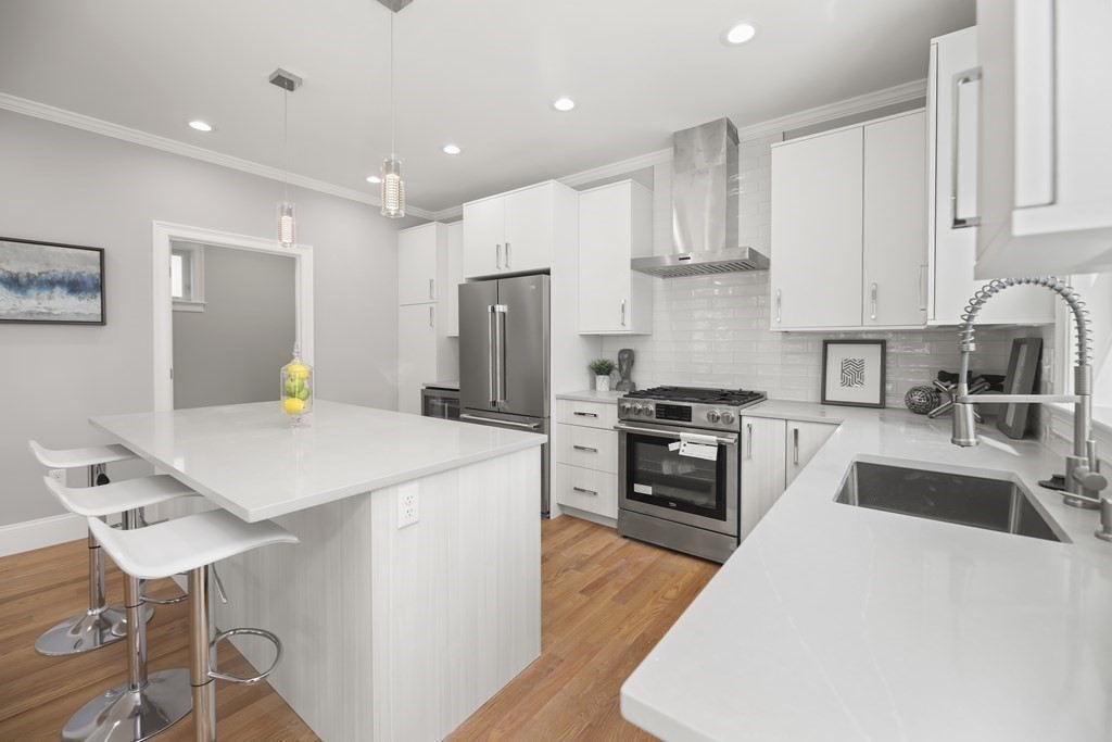 Modern white kitchen with a large island, stainless steel appliances, and warm wood floors.