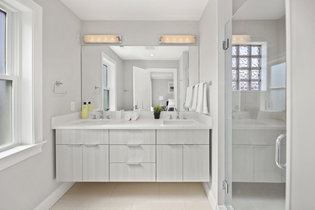 Bright bathroom with a double-sink vanity, large mirror, and glass-enclosed shower.