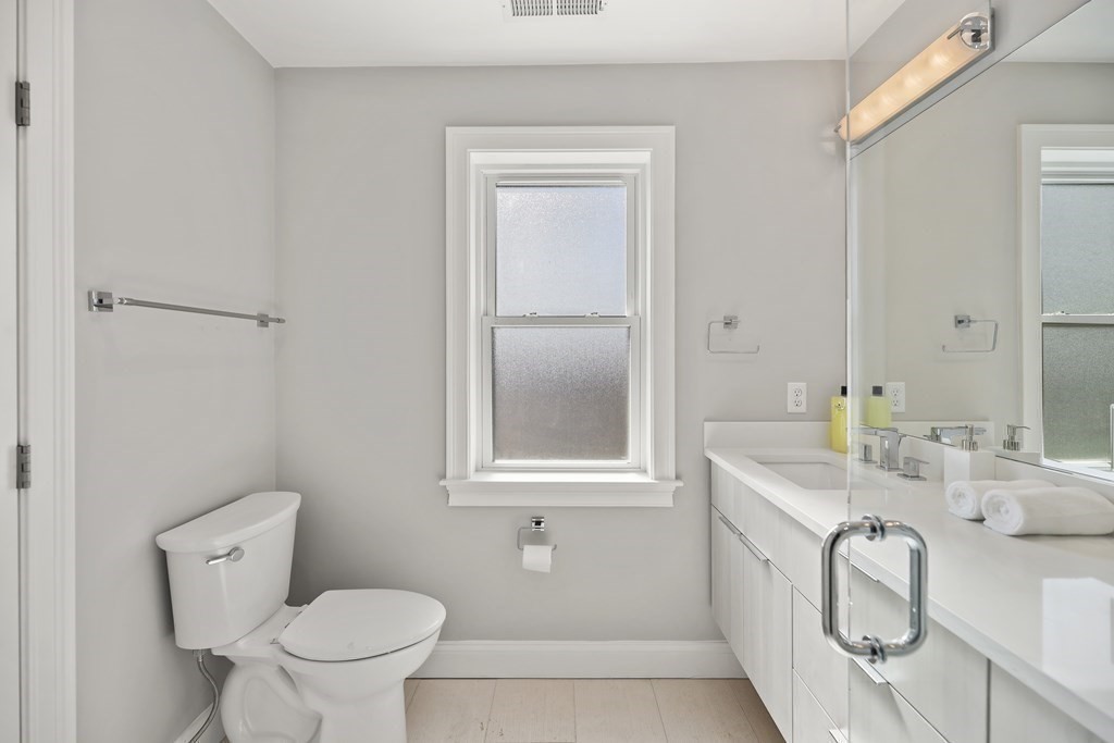 Bathroom with a long white vanity, large mirror, and window with frosted lower glass.