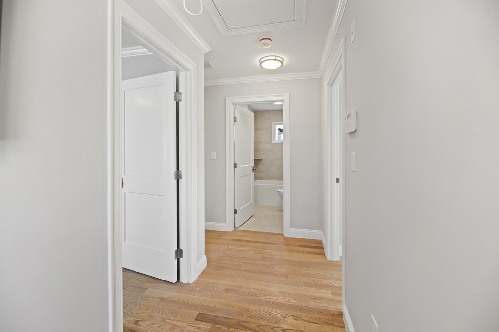Unfurnished hallway with hardwood floors, crown molding, and an open doorway to a bathroom.