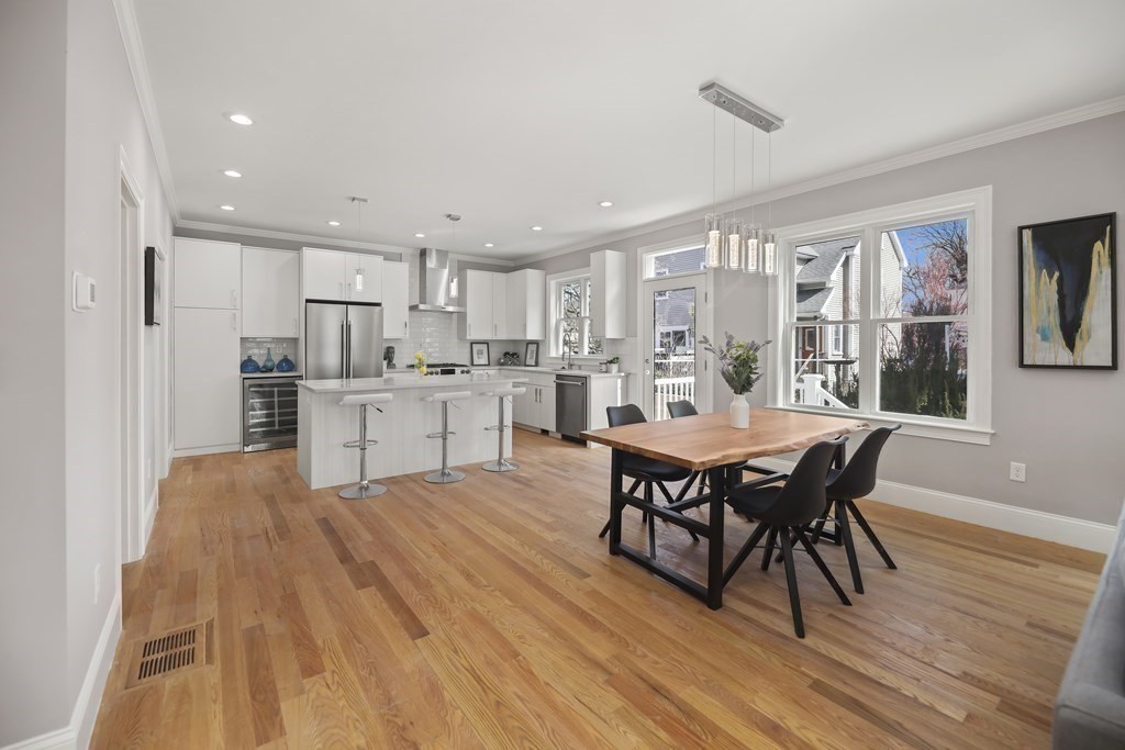 Open kitchen and dining area with a white island, stainless appliances, and hardwood floors.