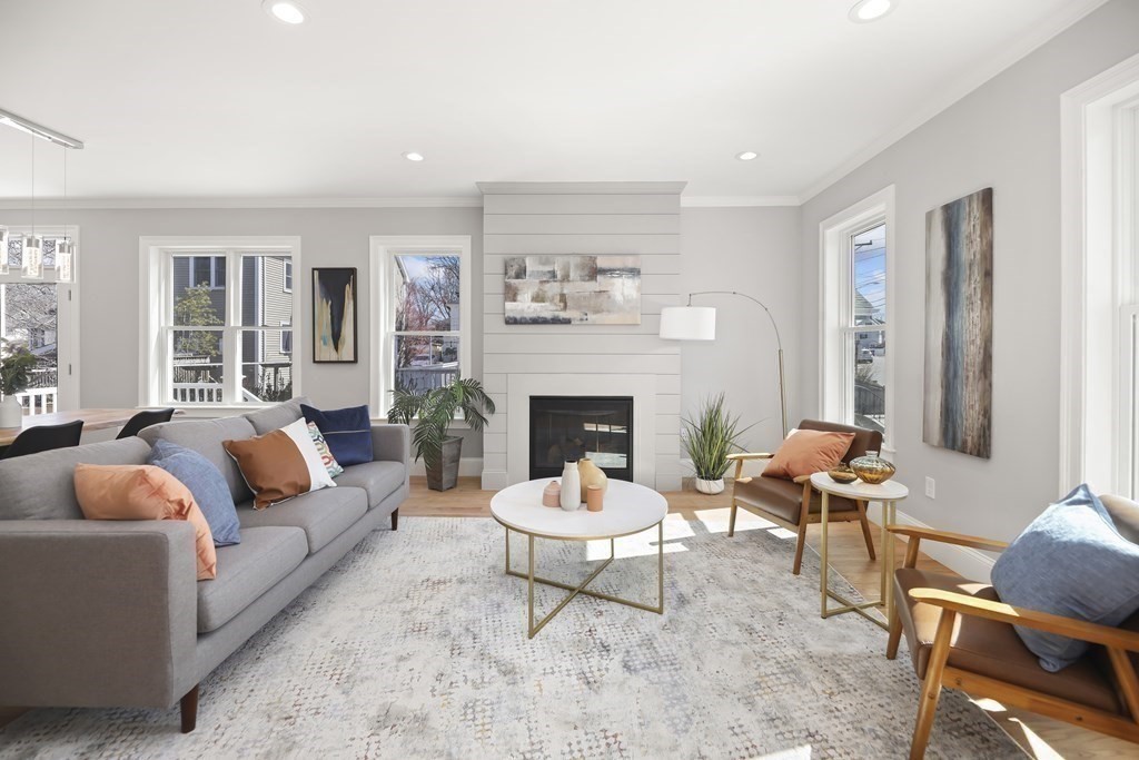 Living room with a shiplap fireplace, gray sectional, leather chairs, and large sunlit windows.