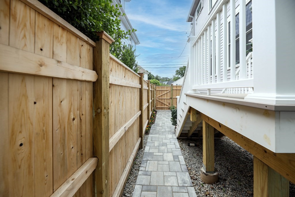 Paver walkway beside a wooden privacy fence and raised white deck.