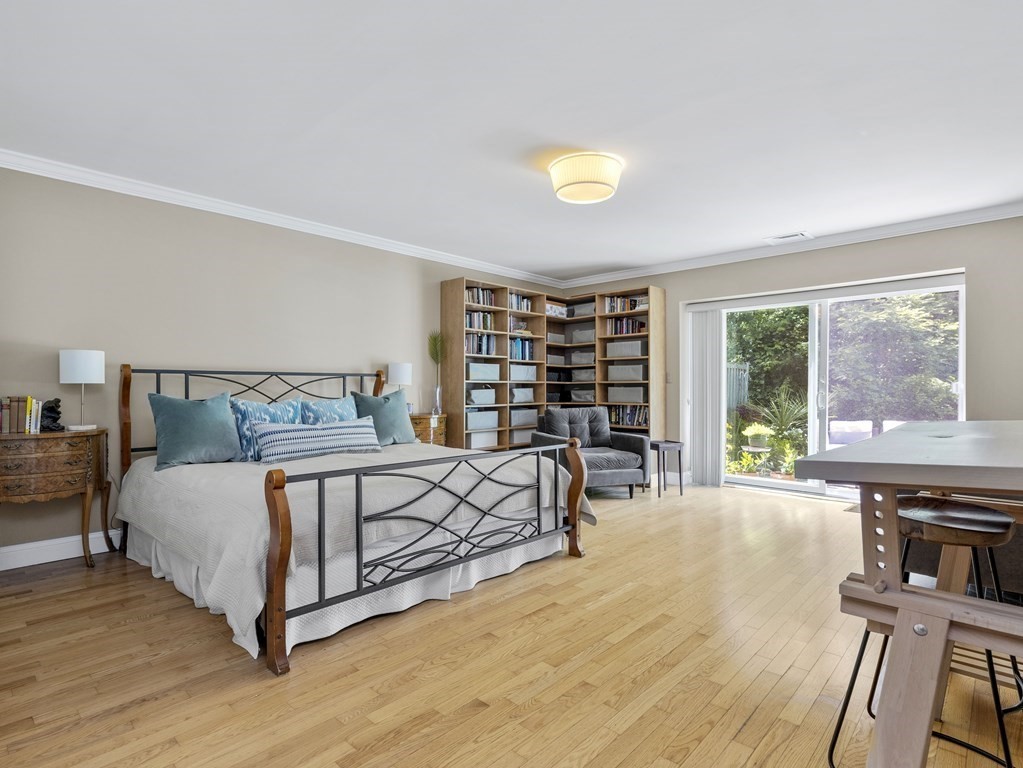 Bedroom with corner bookshelves, hardwood floors, and sliding doors to a leafy garden.