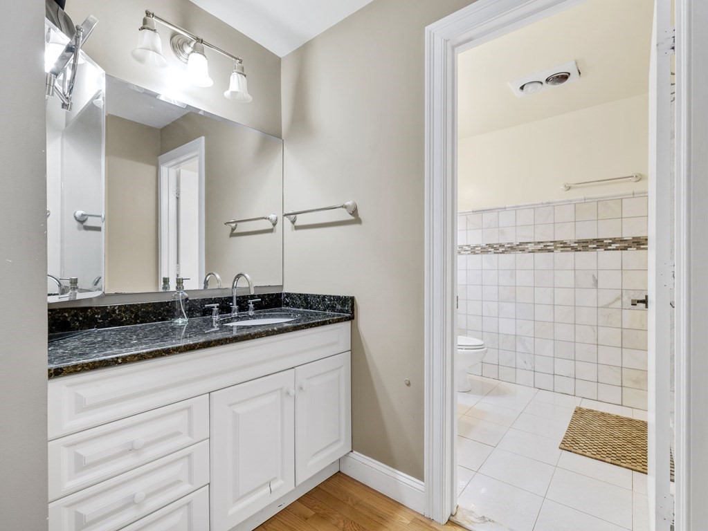 Bathroom vanity with a dark stone countertop beside a tiled shower and toilet area.