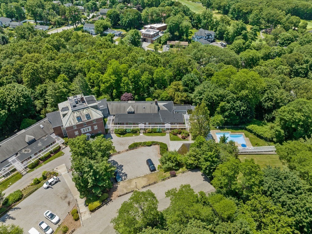 Aerial view of a condominium complex among trees, with a pool and parking areas.