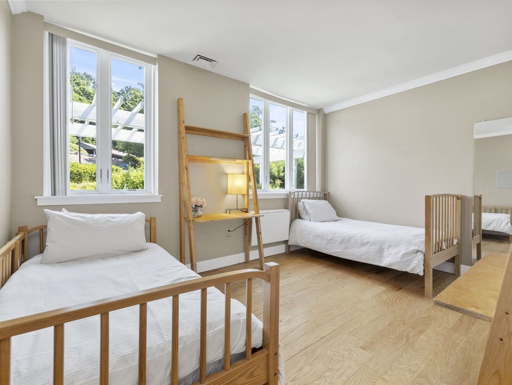 Bedroom with two twin beds, a ladder-style desk, tall windows, and hardwood floors.
