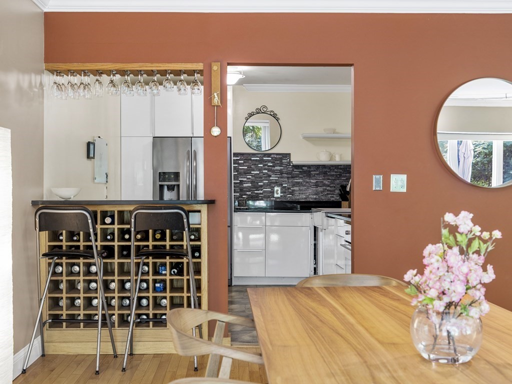 Dining area with a wooden table and wine rack opening onto a white kitchen.