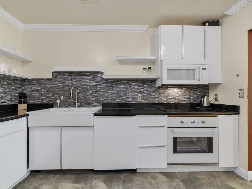 Kitchen with white cabinetry, a farmhouse sink, and dark mosaic backsplash.