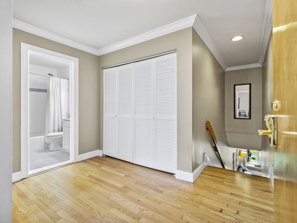 Hallway landing with hardwood floors, louvered closet doors, bathroom doorway, and stairs.