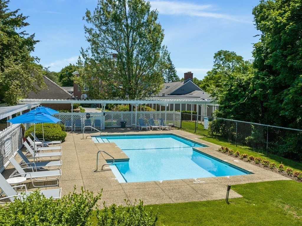 Outdoor pool surrounded by lounge chairs, a white pergola, and mature trees.