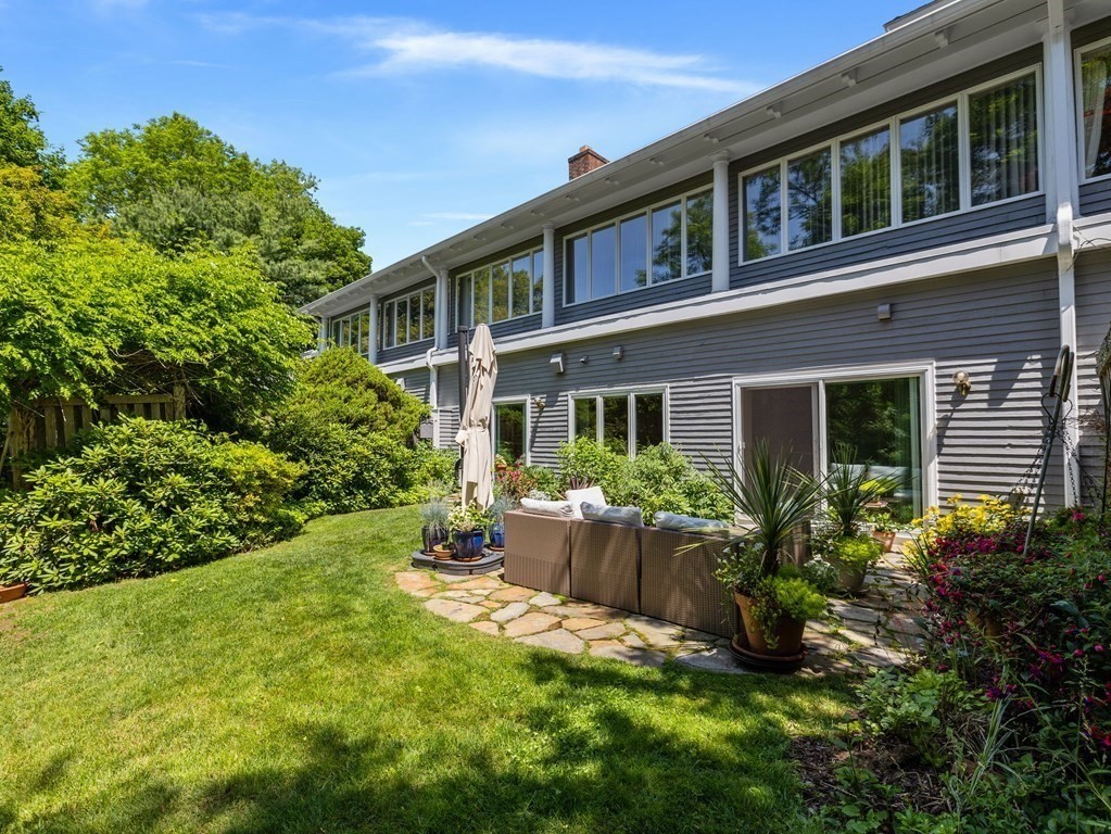 Gray two-story home with a stone patio, outdoor seating, and landscaped lawn.