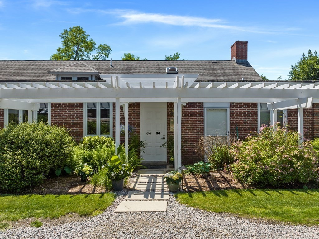 Red-brick residence with a white pergola over its landscaped entrance and walkway.