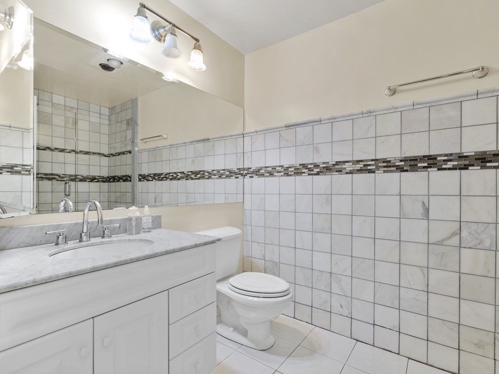 Bathroom with a marble countertop, large mirror, and tiled walls with a dark mosaic accent band.